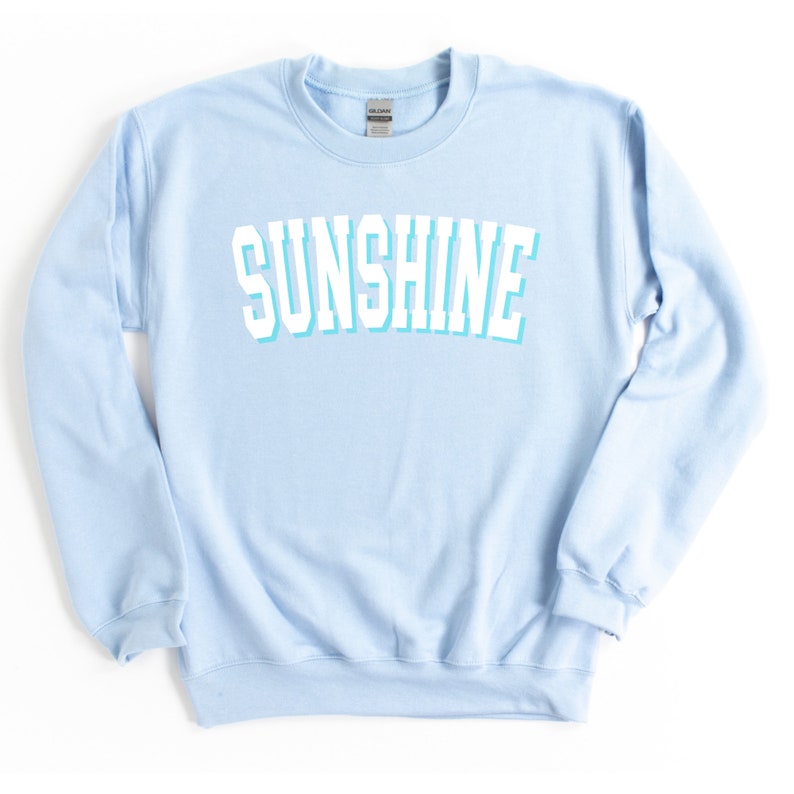 Peut inclure: Un sweat-shirt bleu clair avec le mot "SUNSHINE" imprim&eacute; en blanc avec un contour bleu clair.