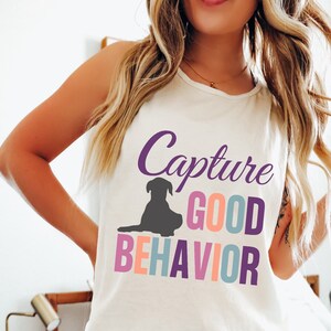 May include: White tank top with a purple, pink, blue, and orange graphic that says "Capture Good Behavior" with a silhouette of a dog sitting down.