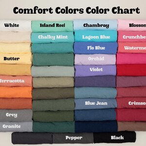 K&ouml;nnte beinhalten: Eine Farbkarte mit Stoffmustern von Comfort Colors. Die Karte enth&auml;lt Farben wie Wei&szlig;, Island Reel, Chambray und Blossom. Jede Farbe ist mit ihrem Namen in wei&szlig;em Text beschriftet.