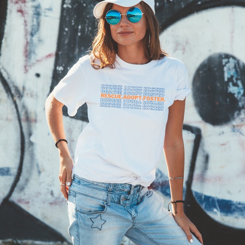 May include: White t-shirt with the text "RESCUE. ADOPT. FOSTER." repeated in a stacked pattern in blue and orange.