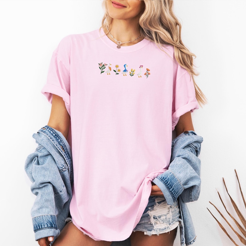 May include: A pink oversized t-shirt with an embroidered design of flowers, ducks, and mushrooms.