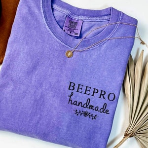 May include: Purple t-shirt with the text "BEEPPRO handmade" in black lettering with a small floral design underneath.