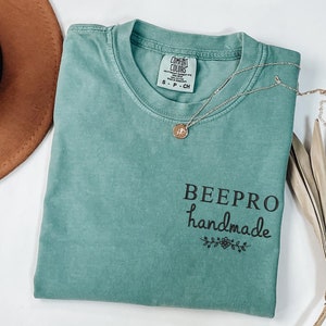 May include: A teal blue t-shirt with the text "BEEPPRO handmade" in black lettering with a small floral design underneath.