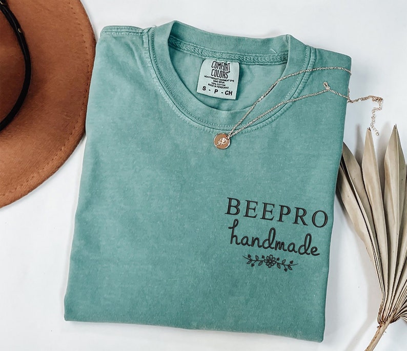May include: A teal blue t-shirt with the text "BEEPPRO handmade" in black lettering with a small floral design underneath.