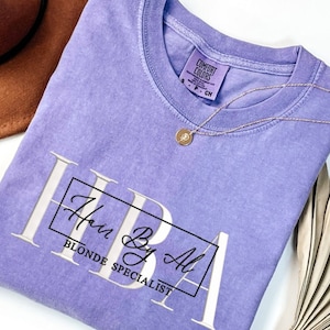 May include: A purple t-shirt with the text "Hair By Al Blonde Specialist" in a white box.