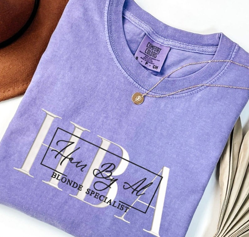 May include: A purple t-shirt with the text "Hair By Al Blonde Specialist" in a white box.