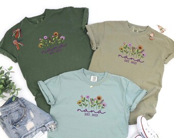 May include: Three t-shirts in different colors with a floral design and the text "nana est. 2023".