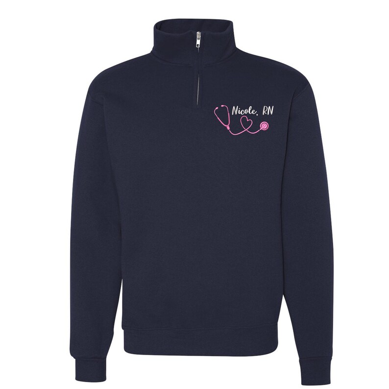 May include: Navy blue quarter-zip sweatshirt with a pink stethoscope and heart graphic and the text "Nicole, RN".