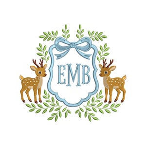 May include: An embroidered design featuring two deer flanking a light blue frame with the initials "EMB". The frame is topped with a bow and surrounded by green leaves. The deer are brown with white spots.