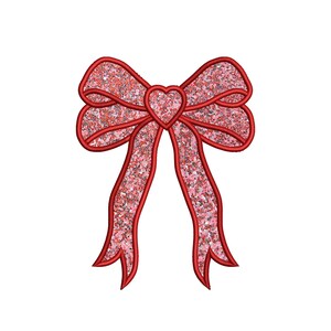 Puede incluir: Un lazo rojo con purpurina con un corazón en el centro. El lazo es un elemento decorativo para manualidades, regalos y otros proyectos.