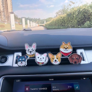 May include: Six different car air fresheners shaped like cartoon dogs. The dogs are a French bulldog, a Shiba Inu, a corgi, a dachshund, a cat, and a schnauzer. The air fresheners are all in different colors and have different expressions on their faces.