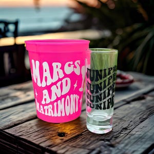 A bright pink plastic, color changing cup and a clear shot glass that is custom and personalized