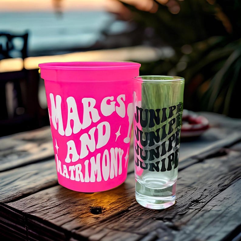 A bright pink plastic, color changing cup and a clear shot glass that is custom and personalized