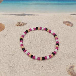 Puede incluir: Una pulsera circular de cuentas con un patr&oacute;n repetitivo de peque&ntilde;as cuentas esf&eacute;ricas y lisas en colores alternos negro, blanco, magenta y bronceado claro. La pulsera presenta un dise&ntilde;o sencillo de una sola hebra sin cierre visible.