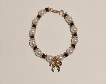 Preciosa pulsera con dije de lazo hecha a mano con perlas, cuentas marrones y doradas.