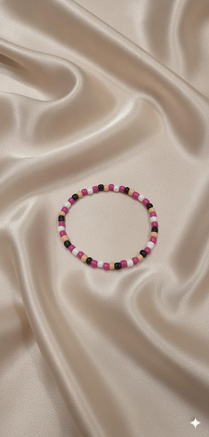 Puede incluir: Una pulsera circular de cuentas que presenta un patr&oacute;n repetitivo de peque&ntilde;as cuentas esf&eacute;ricas y lisas en colores alternos negro, blanco, rosa magenta y un tono beige suave, dispuestas en un bucle continuo sobre una superficie lisa.