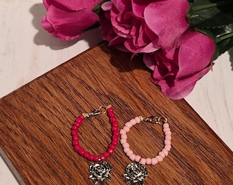 Conjunto artesanal de 2 colgantes para tazas: uno con cuentas rosas y un colgante de llave con forma de flor dorada, y el otro con una cuenta roja. Perfectos para decorar tu taza.