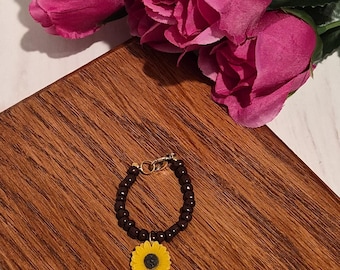 Colgante de copa hecho a mano con cuentas marrones y detalles de flores amarillas, con cierre dorado.