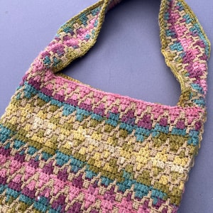 May include: A crocheted bag with a green, pink, and blue striped pattern. The bag has a long strap and is made of a thick, textured yarn.