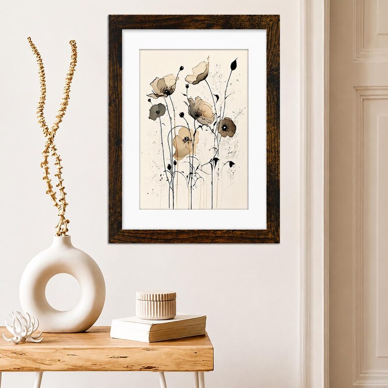May include: A framed wall art print featuring a botanical illustration of delicate poppies in shades of beige, brown, and black on a cream background. The artwork is encased in a dark brown wood-grain frame with a wide white mat border.