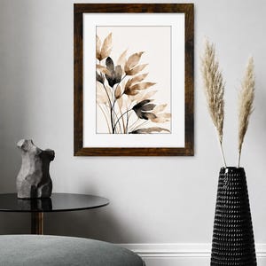 May include: A framed wall art print featuring a watercolor illustration of botanical leaves in shades of brown, beige, and black. The artwork is enclosed in a dark brown wooden frame with a white mat, displaying a cluster of slender, organic foliage.