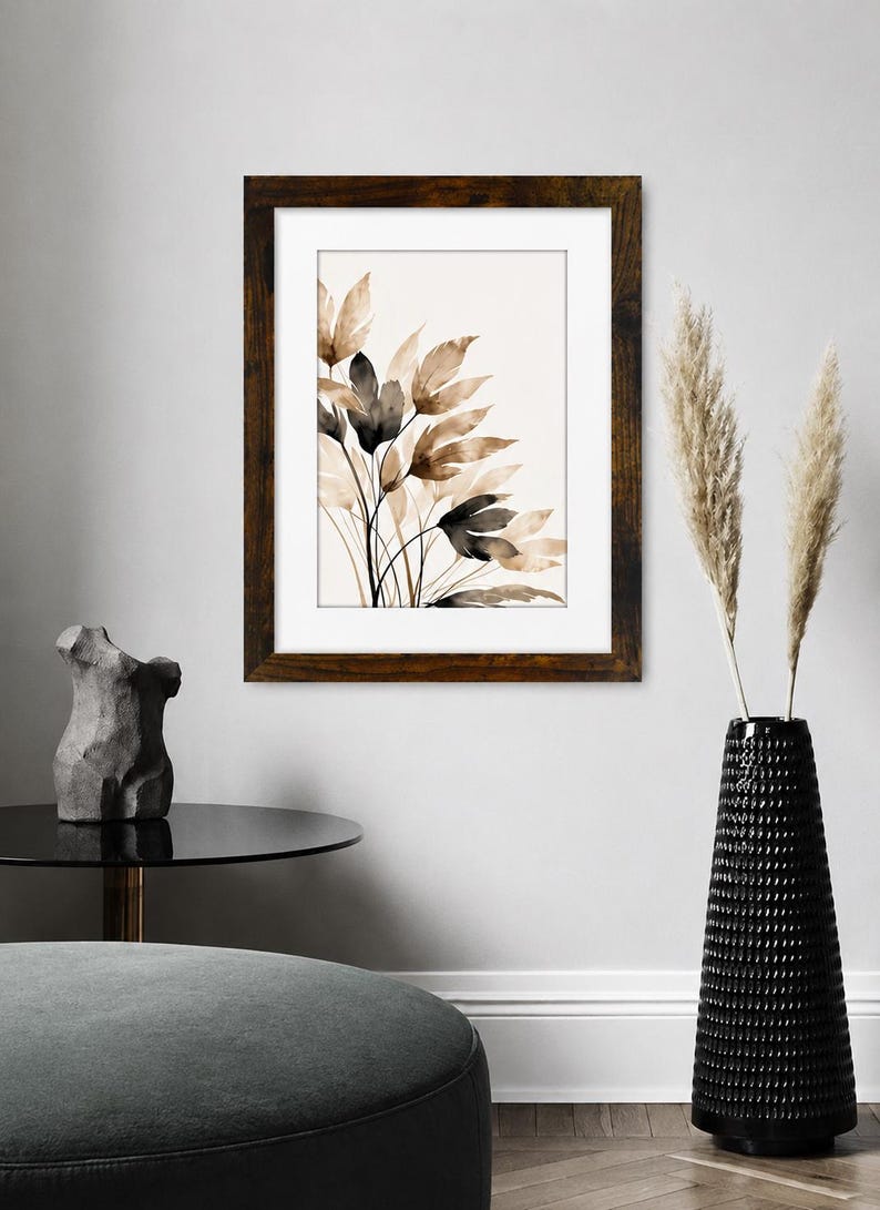May include: A framed wall art print featuring a watercolor illustration of botanical leaves in shades of brown, beige, and black. The artwork is enclosed in a dark brown wooden frame with a white mat, displaying a cluster of slender, organic foliage.