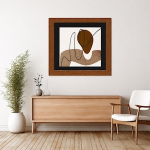 May include: A square framed wall art piece featuring an abstract composition with a dark brown oval, a wavy light brown shape, and a thin black line on a white background, enclosed in a dark wood frame with a black matting border.