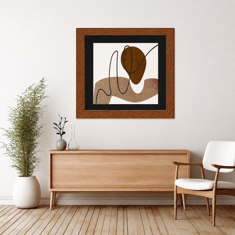 May include: A square framed wall art piece featuring an abstract composition with a dark brown oval, a wavy light brown shape, and a thin black line on a white background, enclosed in a dark wood frame with a black matting border.