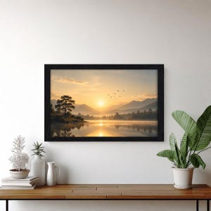 Peut inclure: Une impression d'art paysager rectangulaire dans un cadre noir repr&eacute;sentant un lever de soleil dor&eacute; sur un lac calme, des montagnes lointaines, un arbre solitaire sur la rive et un petit groupe d'oiseaux volant dans le ciel, au-dessus d'une console.