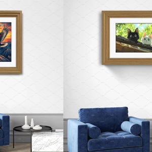 May include: Two framed wall art prints displayed above a blue armchair. The left print shows a bald eagle flying over mountains at sunset. The right print depicts a black cat and a white cat peering over a roof edge amidst green foliage.