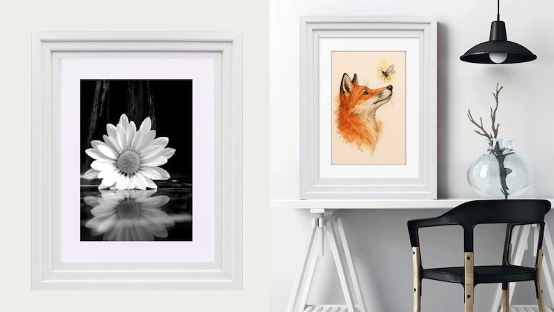May include: Two framed wall art pieces. The left frame contains a black and white photograph of a daisy with a reflection. The right frame features a watercolor illustration of an orange fox looking up at a small bee, displayed on a white desk.