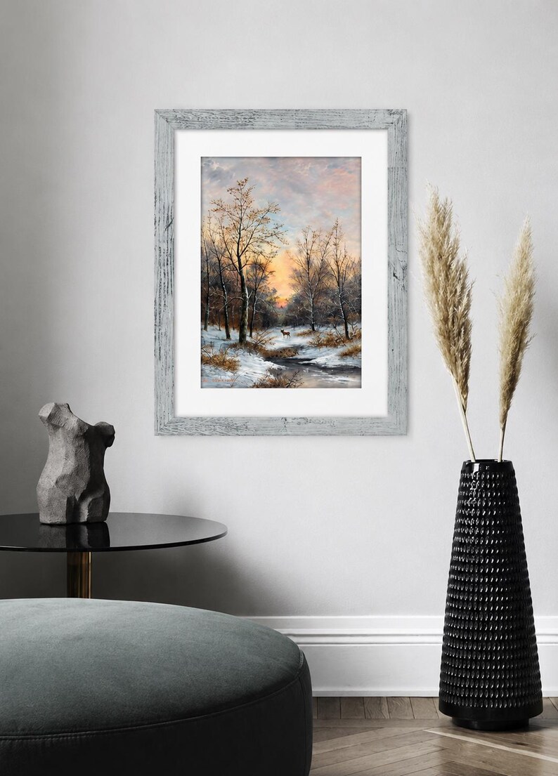 May include: A framed wall art print featuring a winter landscape painting with bare trees, snow-covered ground, a small stream, and a lone deer under a soft orange and blue sunset sky, enclosed in a weathered light gray wooden frame with a white mat.