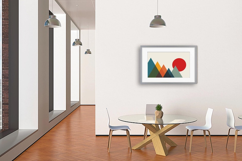 May include: A framed wall art print featuring a geometric mountain landscape with overlapping triangles in shades of teal, green, orange, and dark blue, set against a cream background with a large, solid red circle representing the sun.