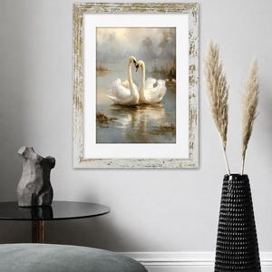 May include: A framed wall art print featuring two white swans swimming on a misty lake, their necks curved to form a heart shape. The artwork is enclosed in a rectangular, distressed white wooden frame with a white mat border.