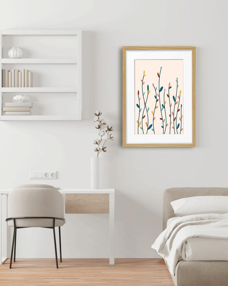May include: A framed wall art print featuring a light cream background with a series of thin, vertical, dark green stems. The stems are adorned with small, scattered, oval-shaped leaves in shades of yellow, teal, pink, and dark red.
