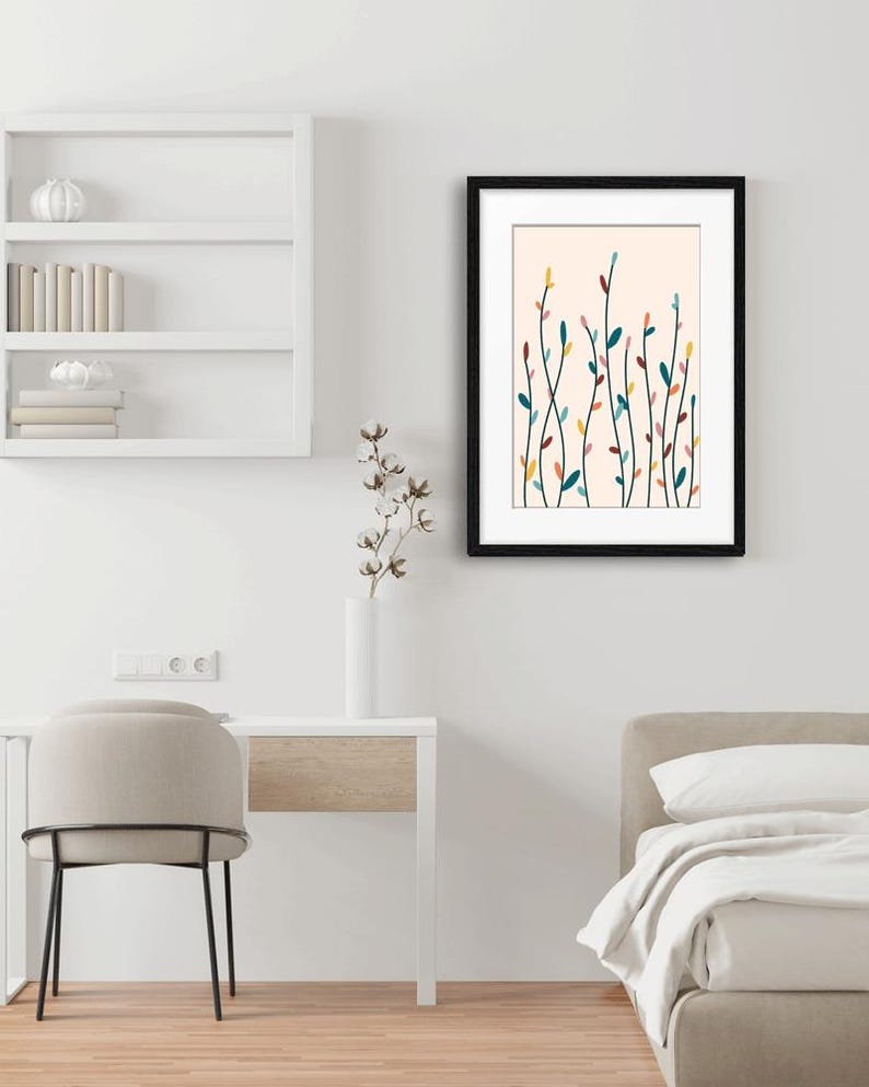 May include: A framed wall art print featuring a botanical illustration of slender, vertical stems with small, colorful leaves in shades of teal, yellow, and muted pink against a pale cream background, enclosed in a simple black rectangular frame.