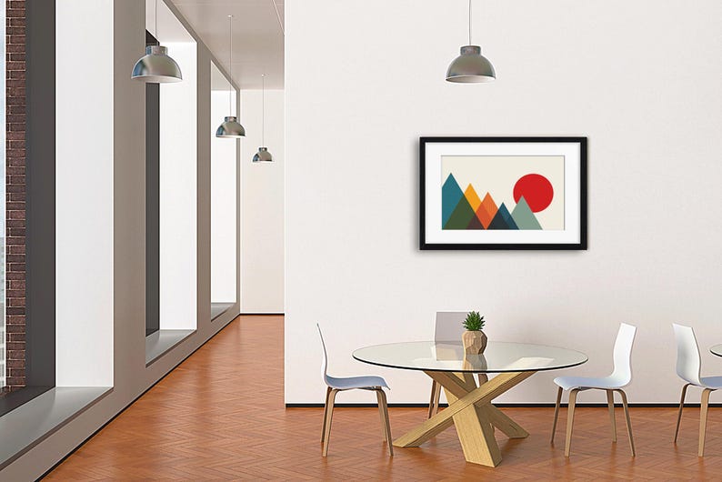 May include: A framed wall art print featuring a geometric mountain landscape with overlapping triangles in shades of blue, green, orange, and yellow, set against a cream background with a large solid red circle representing a sun in the sky.