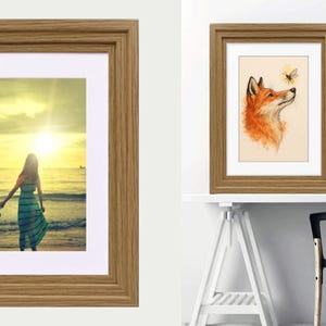 May include: A rectangular picture frame with a light brown wood grain finish and a white mat border. The frame displays a photograph of a person standing on a beach at sunset, and another version shows an illustration of a fox looking at a bee.
