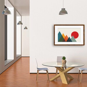 May include: A framed wall art print featuring a geometric mountain landscape with overlapping triangles in shades of blue, green, and orange, set against a cream background with a large, solid red circle representing a sun in the upper right corner.