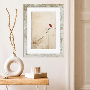May include: A framed wall art print featuring a bright red cardinal bird perched on a thin, dark branch with small red berries against a textured, cream-colored background. The artwork is enclosed in a distressed, weathered white wooden frame.