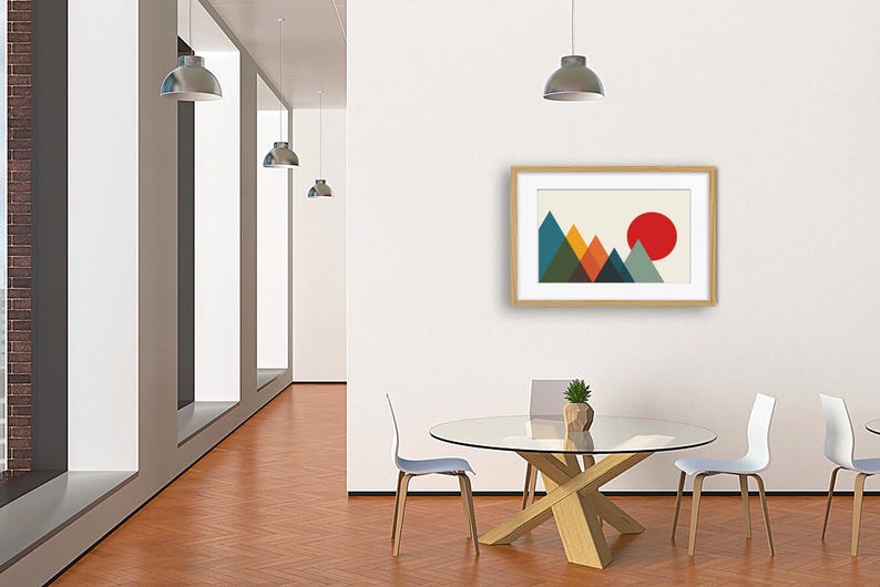 May include: A framed wall art print featuring a geometric mountain landscape with overlapping triangles in shades of teal, orange, dark blue, and olive green, set against a cream background with a large solid red circle representing the sun.
