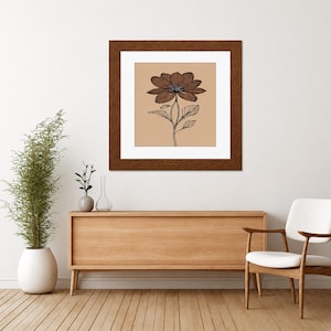 May include: A square framed wall art piece featuring a black line drawing of a single flower with detailed petals and leaves centered on a solid tan background. The artwork is enclosed in a dark brown wooden frame with a white mat border.