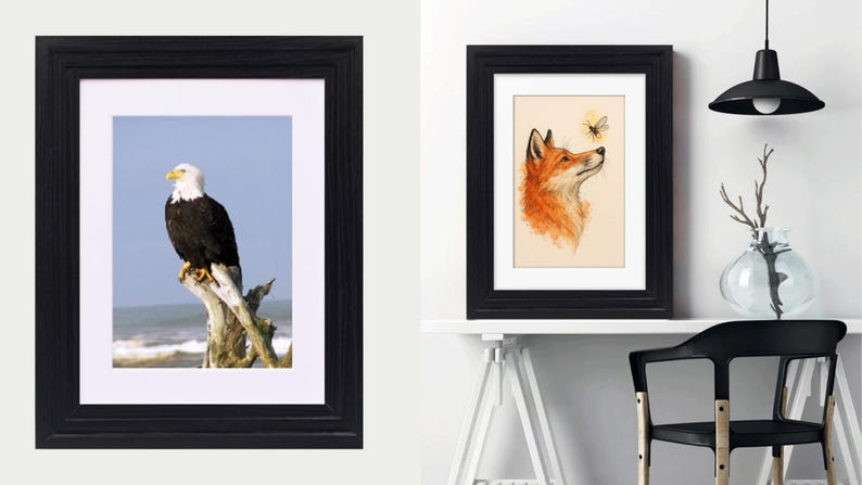 May include: Two black rectangular frames with white matting. The left frame displays a bald eagle perched on a weathered tree stump against a blue sky and ocean. The right frame contains a watercolor illustration of a fox looking at a small bee.