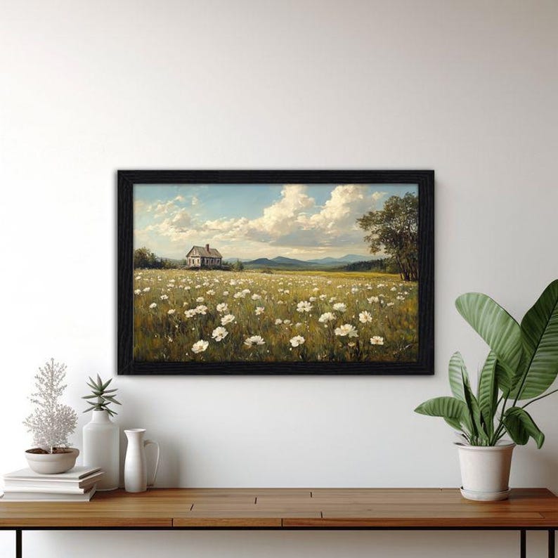 Peut inclure: Une peinture de paysage rectangulaire dans un cadre noir repr&eacute;sentant une petite maison situ&eacute;e dans un vaste champ de fleurs blanches sous un ciel bleu avec des nuages blancs. La sc&egrave;ne inclut des collines lointaines et un grand arbre.
