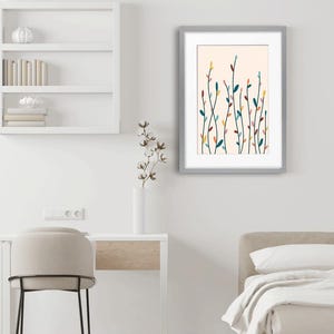May include: A framed wall art print featuring a light peach background with vertical, slender stems and small, multi-colored leaves in shades of teal, yellow, pink, and dark brown. The artwork is enclosed in a simple, light gray rectangular frame.