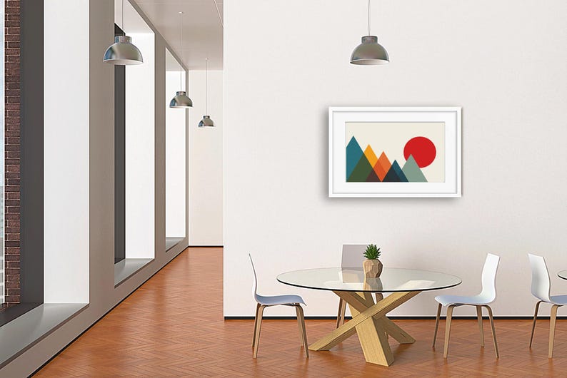 May include: A framed wall art print featuring a geometric mountain landscape with overlapping triangles in shades of teal, green, orange, and dark blue, set against a cream background with a large solid red circle representing the sun.