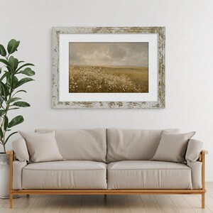 May include: A landscape painting in a distressed white wooden frame featuring a field of white wildflowers under a cloudy, muted sky. The artwork is displayed in a horizontal orientation with a white mat border, showcasing earthy tones and soft textures.