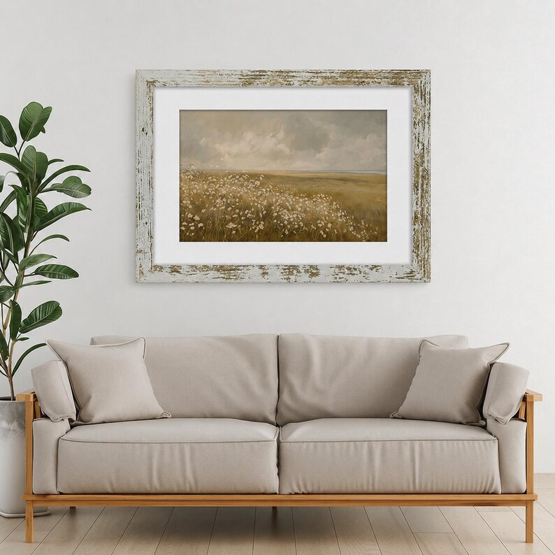 May include: A landscape painting in a distressed white wooden frame featuring a field of white wildflowers under a cloudy, muted sky. The artwork is displayed in a horizontal orientation with a white mat border, showcasing earthy tones and soft textures.