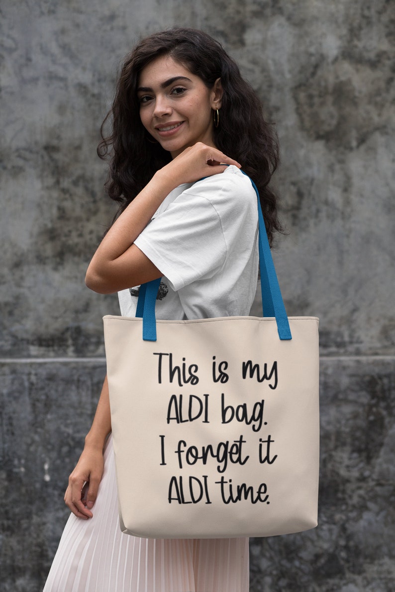 Op de afbeelding: Een witte canvas tote bag met blauwe handvatten. De tas heeft zwarte tekst die "This is my ALDI bag. I forget it ALDI time." zegt.