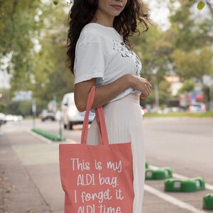 Op de afbeelding: Een koraalkleurige tote bag met witte tekst die "This is my ALDI bag. I forget it ALDI time." zegt.